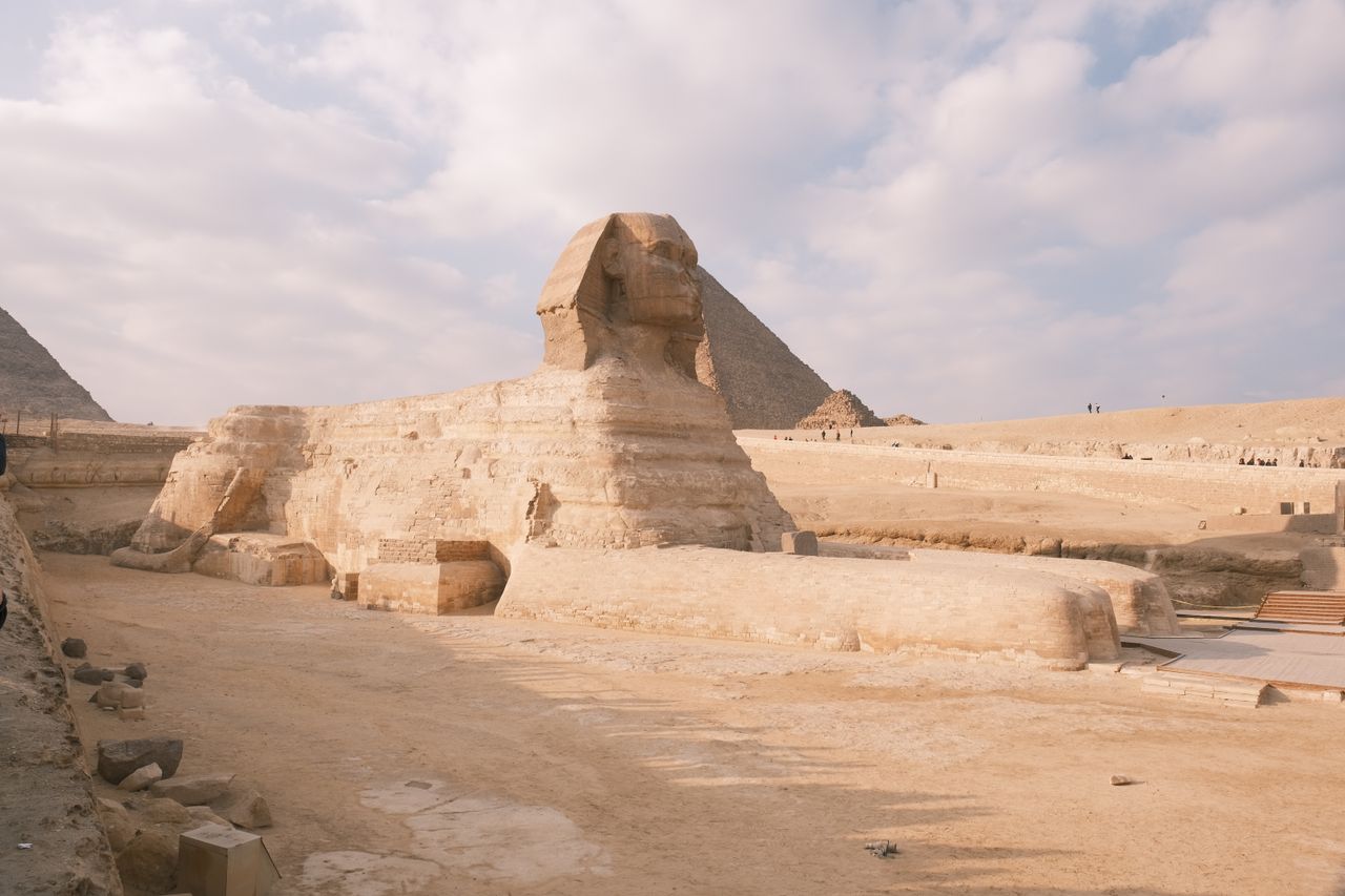 Voyage sur-mesure Egypte The Great Sphinx of Giza against a backdrop of pyramids and a partly cloudy sky.